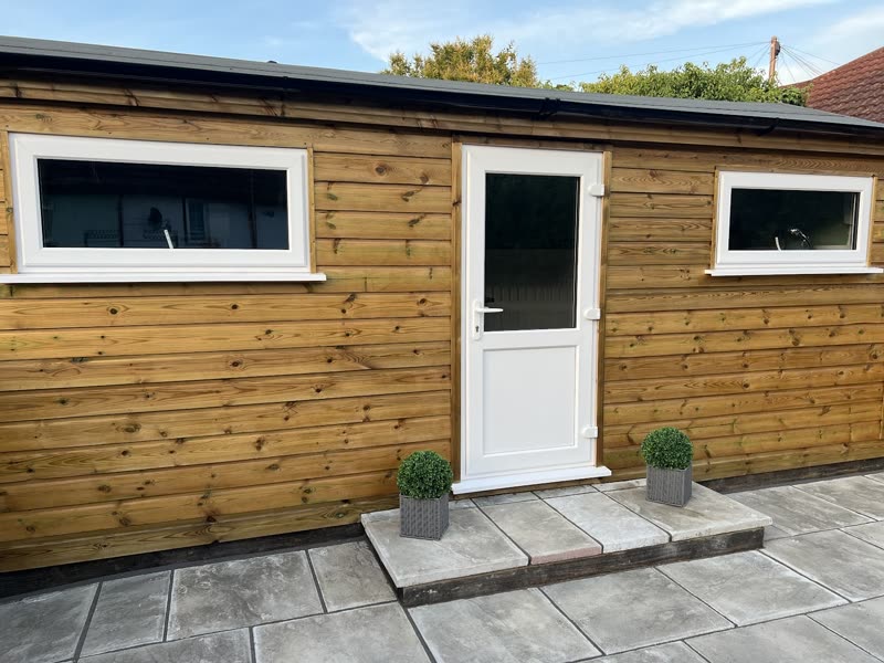 The timber-clad grooming cabin at Barking Barbers, with a white door, paved step and two potted shrubs